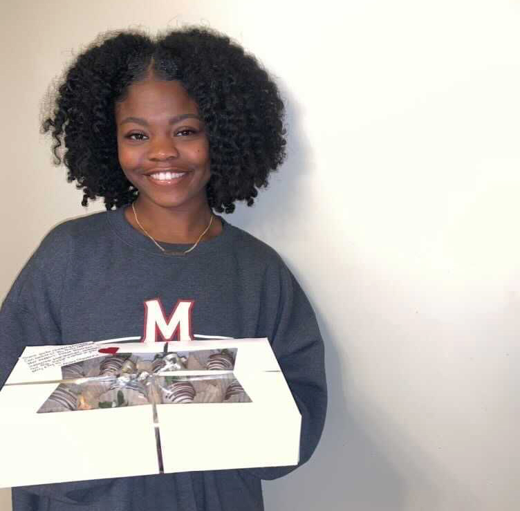 A person holding a box of chocolate covered strawberries and other sweets